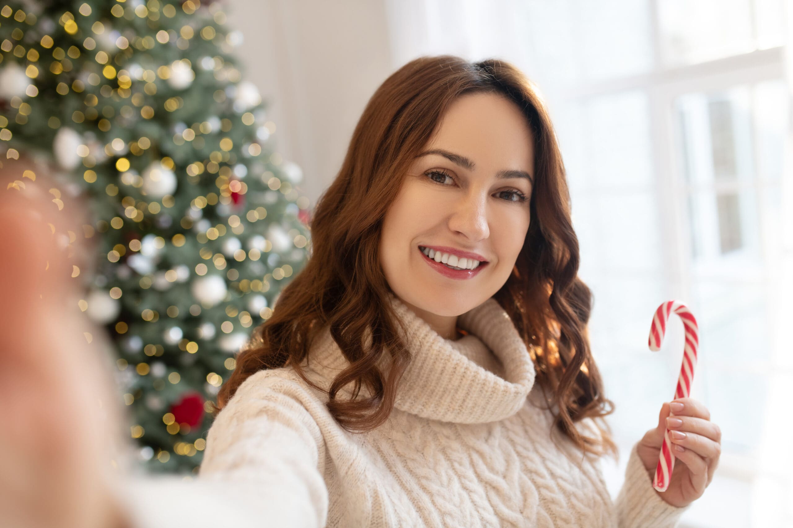 Dark-haired woman near christmas tree making selfie