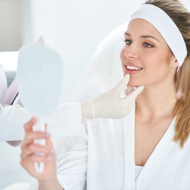 Woman looking at her medical spa treatment results in a handheld mirror